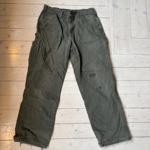 Gröna workpant cargobyxor från Carhartt - Säljer ett par gröna cargobyxor från Carhartt i bra skick. De har en baggy passform och flera praktiska fickor. Lite slitna men lagade vilket får dem att se extra feta ut 🙌Perfekta för höst och vår, med en slitstark design som funkar för både vardag och utomhusaktiviteter. Byxorna har en klassisk look med Carhartt-logga på bakfickan.