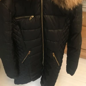 Svart quiltad jacka från Rockandblue - Säljer en svart quiltad jacka från Rockandblue i mycket bra skick. Den har en mysig pälsdetalj på huvan och flera praktiska dragkedjor i guld. Perfekt för kalla vinterdagar! 🖤