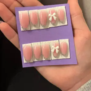 Säljer ett set med superfina handgjorda press on nails,gjorda av HEMA fri gelé. Ringfinger-naglarna har en söt vit rosett som detalj. Settet kommer med en rosa nagelfil,en liten pinne att putta bak nagelbanden med,ett litet kort där det står instruktioner hur du fäster naglarna,klister lappar som du sätter på naglarna så de fäster,och du får även med en rosa ”luddfri nail wipe” som du kan ta lite nagellacks borttagning på,för att få bort fildammet efter att du filat nagelytan. Storlek S/M