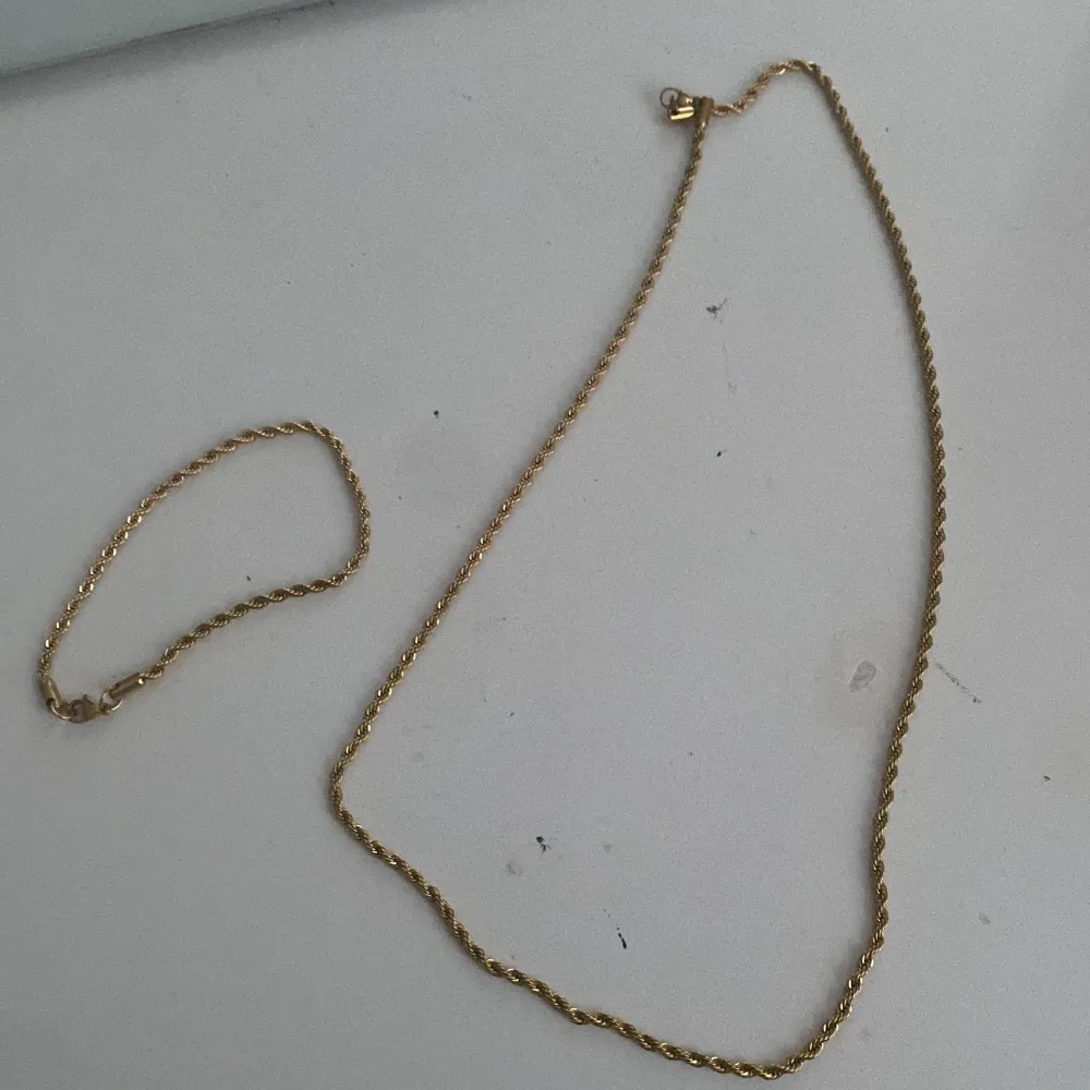 Elegant set med ett guldhalsband och matchande armband. Halsbandet har en fin vriden design. Perfekt för att ge en touch av lyx till din outfit.. Asusteet.