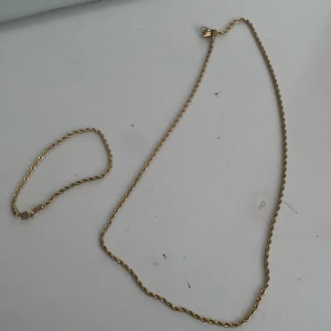 Guldhalsband och armband - Elegant set med ett guldhalsband och matchande armband. Halsbandet har en fin vriden design. Perfekt för att ge en touch av lyx till din outfit.