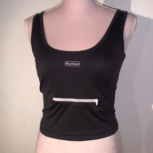 Svart linnetopp från Beachwave - Snygg svart linnetopp från Beachwave med en praktisk dragkedjeficka framtill. Perfekt för att bära småsaker. Toppen är ärmlös och har en tight passform. Storlek XS. För bara 25kr. 