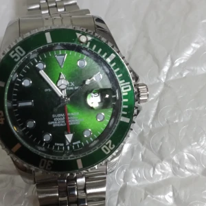 En klocka från R. Grön dykarur med silverarmband - Snygg dykarur med grön urtavla och silverfärgat armband. Klockan har tydliga markeringar och en vridbar bezel. Perfekt för den som gillar en sportig stil.