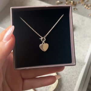 Silverhalsband med hjärthänge - Elegant silverhalsband med ett litet hjärthänge. Perfekt för att lägga till en subtil touch av stil till din outfit. Kedjan är tunn och smidig, vilket gör den bekväm att bära hela dagen.
