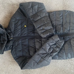 Svart jacka från Lyle & Scott, junior strl 12-13 år - Säljer en svart tunn dunjacka med luva från Lyle & Scott. Väldigt fint skick och knappt använd. Strl junior 12-13 år. 