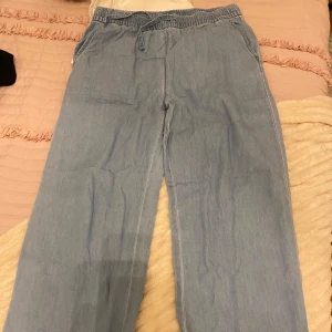 Ljusblå byxor med resårmidja - Säljer ett par ljusblå byxor med resårmidja och avslappnad passform. Byxorna har fickor på sidorna och är perfekta för en bekväm stil. De är tillverkade i ett lätt material som ger en skön känsla. Det är ett par linnebyxor 