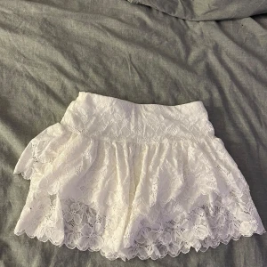 Vit spetskjol från Shein - Säljer en söt vit spetskjol från Shein i storlek XS. Kjolen har ett vackert spetsmönster och volanger som ger en romantisk känsla. Perfekt för att skapa en feminin look. 🕊️ Inbyggda shorts