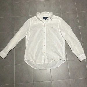 Vit långärmad skjorta från Ralph Lauren - Klassisk vit skjorta från Ralph Lauren med broderad logga på bröstet. Skjortan har långa ärmar och knappar framtill. Perfekt för en stilren look. Skjortan är också i 100% linne och är storleken 14-16 år, alltså large i barnstorlek. Inga som helst deflekter på skjortan och är väl omhändetagen och är sparsamt använd. Skriv vid funderingar!!