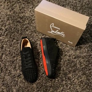 Christian Louboutin - Helt nya svarta sneakers från Christian Louboutin med nitar på ovansidan och den ikoniska röda sulan. Skorna har snörning och är tillverkade i mocka. Skorna är storlek 43. Skolåda + tillbehör ingår i köpet!
