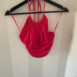 Halterneck topp - Trendig rosa axelbandslös topp från Gina med knytband i nacken. Toppen har en draperad design och är perfekt för en somrig look.