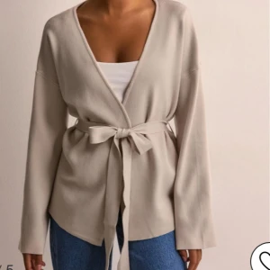 Beige omlottjacka från Nelly - Säljer denna omlottkoftan från nelly- OBJREYNARD L/S CARDIGAN NOOS, då den inte har kommit till användning. Jätte skön i materialet!!  Nypris 600kr