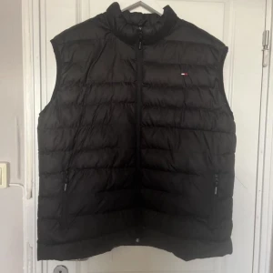 Svart dunväst från Tommy Hilfiger - Snygg svart dunväst från Tommy Hilfiger med dragkedja och diskret logga på bröstet. Perfekt för kyligare dagar och enkel att matcha med andra plagg.