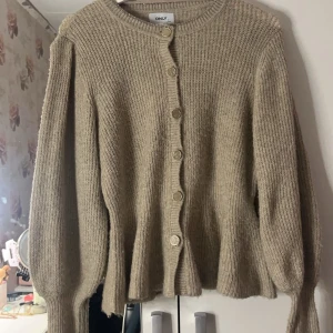 Beige stickad kofta från ONLY - Säljer en beige stickad kofta från ONLY med knappar framtill. Koftan har långa ärmar och en ribbad struktur som ger en mysig känsla. Perfekt för kyligare dagar.