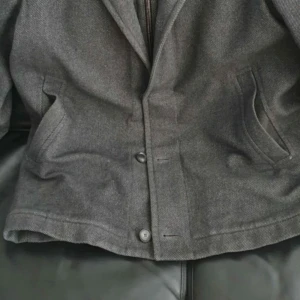 Grå kappa från Hugo Boss - Snygg grå kappa från Hugo Boss med klassisk design. Jackan har knappar framtill och praktiska fickor på sidorna. Perfekt för kyligare dagar med sin stilrena look.