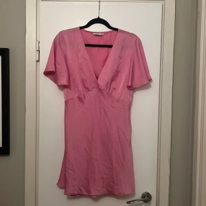 Rosa klänning från Stradivarius - Snygg rosa klänning från Stradivarius med v-ringning och korta ärmar. Perfekt för en somrig look. Klänningen har en smickrande passform och är tillverkad i ett lätt material.