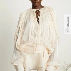 MISS ROSSIER KLÄNNING - Elegant champagnefärgad klänning med volangdetaljer och långärmad design. Klänningen har en lös passform med knytning vid halsen och en kort kjol med volanger. Perfekt för en stilfull look. Från miss rossier aldrig använt super fin!!!! Ger isabel marant vibes ny pris 1800