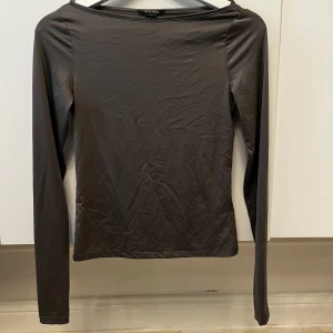 Grå långärmad topp  - Snygg grå boatneck topp. Perfekt för en stilren look. Tillverkad i ett mjukt och bekvämt material som passar bra till olika outfits.