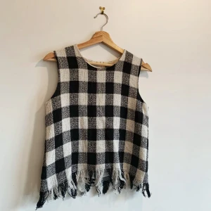 Rutig topp från Zara Basic Collection - Säljer en stilren rutig topp från Zara Basic Collection i svart och beige. Toppen har fransar längst ner och är perfekt för en trendig look. Den är ärmlös och har en klassisk rund halsringning.