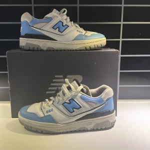 New Balance 550 i blå och vit - Säljer ett par New Balance 550 sneakers i en snygg kombination av blått och vitt. Skorna har en klassisk design med snörning och New Balance-loggan på sidan. Perfekta för en stilren och sportig look.