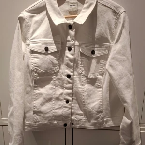 Vit jeansjacka från ONLY - Snygg vit jeansjacka från ONLY med klassisk design. Jackan har knappar framtill och två bröstfickor med lock och knapp. Perfekt för en stilren look.