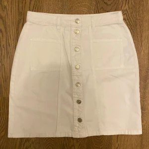 Vit kjol med knappar från edc - Snygg vit kjol från edc med knappar framtill och praktiska fickor. Perfekt för en stilren look. Kjolen har en klassisk design med bälteshällor och är i en bekväm passform.