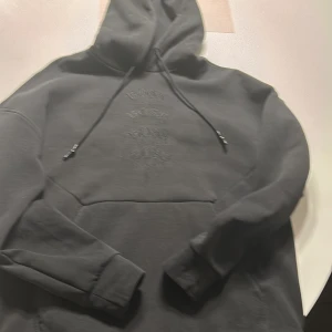 Svart hoodie från Hugo Boss - Snygg svart hoodie från Hugo Boss med broderad logotyp på bröstet. Den har en klassisk design med dragsko i huvan och en stor magficka. 