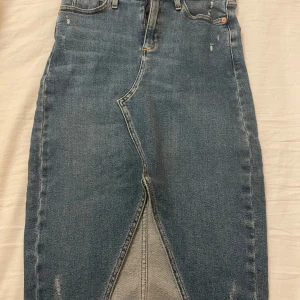 Jeanskjol från River Island väldig stretchig - Snygg jeanskjol från River Island i klassisk blå denim. Kjolen har en stilren design med femficksmodell och en subtil slits framtill. Perfekt för en avslappnad look. Finns inte längre kvar!!