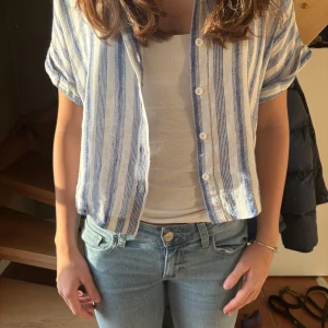 Randig kortärmad skjorta - Säljer en stilren randig skjorta i blått och vitt med korta ärmar och knappar framtill. Perfekt topp både knäppt eller öppen med något under.🔥🔥använd få gånger. Och säljer för den är för liten nu💕