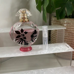 2ml‼️Paco rabanne Olympeaflora - Elegant parfymflaska med blommigt mönster i svart och rosa. Flaskan har en rund form med en dekorativ kork i guld och transparent plast. Perfekt för den som älskar en lyxig och feminin doft.