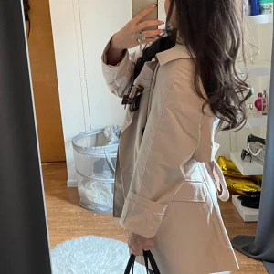 Beige trenchcoat - Snygg beige trenchcoat med klassisk design och knytbälte i midjan. Perfekt för vår och höst. Långärmad med stilrena detaljer🍁🍁🍂🍂