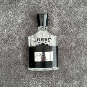 Creed Aventus Parfym - Säljer en exklusiv Creed Aventus parfym i en elegant glasflaska med svart etikett och silverfärgad kork. Flaskan rymmer 100 ml och är tillverkad i Frankrike. Perfekt för den som söker en lyxig doftupplevelse. Köpt från Sephora.