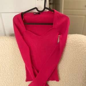 Rosa ribbad tröja från Gina Tricot - Snygg rosa ribbad tröja från Gina Tricot med en v-ringad design. Tröjan har långa ärmar och en figurnära passform som passar perfekt för både vardag och speciella tillfällen.
