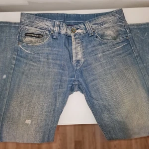 Blå jeans med slitna detaljer - Snygga blå jeans från RG512 med en cool slitningseffekt. Vanligt slitage. Perfekta för en avslappnad stil. Garderobsrensning så kika gärna på övriga auktioner.