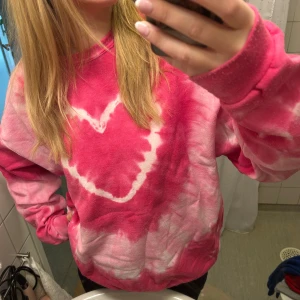 Rosa sweatshirt - Säljer en rosa batikmönstrad tröja med ett vitt hjärta på framsidan. Tröjan är endast använd fåtal gånger och finns ej att köpa längre.