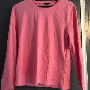 Rosa långärmad tröja - Säljer en enkel och stilren rosa långärmad tröja. Perfekt för en avslappnad look. Tröjan har en rund halsringning och är gjord i ett mjukt material.