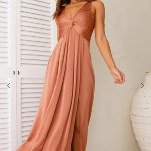 Rostfärgad klänning, cocktail, fest, balklänning, öppen rygg - Rostfärgad lång klänning, tyvärr för liten för mig och därför aldrig använd. Rätt stretchig i ryggen, resårband och knytning. Längd från axelbandet och ned är ca 139cm. Nypris, 1400kr