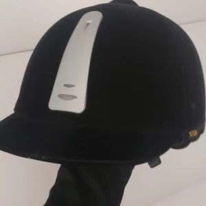 Svart ridhjälm från Kylin - Snygg svart ridhjälm från Kylin med en elegant silverdetalj framtill. Hjälmen har en slät yta och justerbar passform för optimal komfort. Perfekt för ridning och säkerhet. Inte haft någon avrammling eller hårtfall mit hjälmen💕