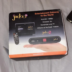 Jadoo TV Jadoo2 Streaming Box - Säljer en Jadoo TV Jadoo2 streaming box som erbjuder Full HD 1080p streaming. Den har stöd för trådlöst internet och ger tillgång till global live-TV och miljontals YouTube-videor. Inkluderar fjärrkontroll, HDMI-kabel, RCA-kabel, strömadapter, Ethernet-kabel och trådlös USB-adapter.