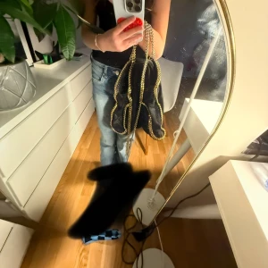 Svart väska Stella macartny - Kan mötas upp ❤️Snygg svart väska från Stella McCartney med guldiga kedjedetaljer. Väskan har en rund metallbricka med logotyp och en rymlig insida med dragkedja. Perfekt för att ge din outfit en lyxig touch.