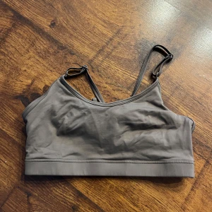 Brunbeige sporttopp från Casall - Säljer en brungrå sporttopp från Casall med justerbara axelband och elastisk kant för extra stöd. Perfekt för träning och bekväm passform. Toppen har en stilren design med Casall-logga på baksidan och snygga band