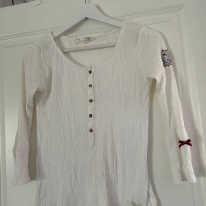 Vit ribbad tröja från Odd Molly - Säljer en vit ribbad tröja från Odd Molly med långa ärmar och knappar framtill. Fin spetskant längs med halskragen. Tröjan har en broderad detalj på ärmen och en liten rosett. Perfekt för en stilren och bekväm look. Tröjan är i fint skick samt sparsamt använd. Vid frågor och funderingar hör av er, jag svarar så fort jag kan!🩷