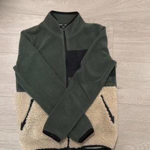 Grön fleecejacka med teddyfoder - Säljer en grön fleecejacka med beige teddyfoder. Jackan har en dragkedja framtill och en bröstficka i svart. Perfekt för kommande våren. Size: XS eller 160 cm