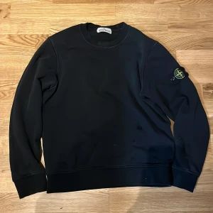 Svart tröja från Stone Island - Säljer en stilren svart tröja från Stone Island med deras ikoniska märke på ärmen. Perfekt för en casual look. Tröjan har rund hals och långa ärmar.