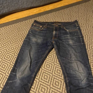 Blå jeans från Nudie Jeans - Säljer ett par snygga blå jeans från Nudie Jeans. De har en klassisk femficksdesign med orange sömmar och en knappgylf. Perfekta för en avslappnad stil. De är 34 men passar 32-32 ja har 32 och använde dessa.två klädesplagg till följer 