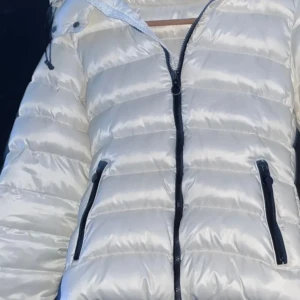 Vit dunjacka från Moncler - Snygg vit dunjacka från Moncler med huva och dragkedja. Jackan har långa ärmar och praktiska fickor med dragkedja. Perfekt för kyliga dagar när du vill hålla stilen. 🧥✨