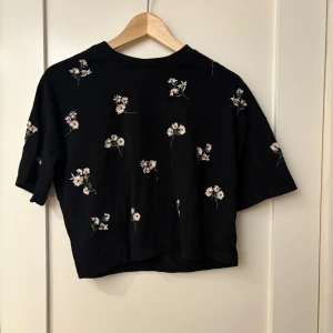 Svart blommig topp från ASOS - Säljer en svart topp från ASOS med söta blommiga mönster. Toppen har korta ärmar och en avslappnad passform. Perfekt för en somrig look! 🌸
