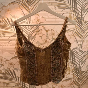 Broderad korsettopp i grön - Säljer en vacker korsettopp i grön med intrikata broderier och breda axelband. Toppen har en elegant design med detaljerade mönster i tyget som ger en lyxig känsla.