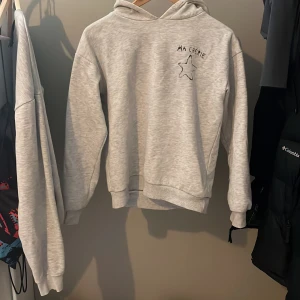 Grå hoodie från Gina Tricot - Säljer en grå hoodie från Gina Tricot med texten 'Ma Chérie' och en stjärna tryckt på framsidan. Perfekt för en avslappnad stil. Hoodien har långa ärmar och en klassisk huva. Skön och stilren design för alla tillfällen. Säljer pga av för liten storlek 146/152