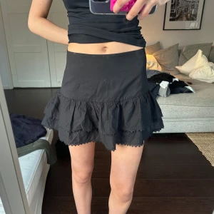 Svart volangkjol - Snygg svart kortkjol med volanger. Perfekt för en trendig look. Kjolen har en enkel design med flera lager volanger som ger en fin rörelse. 💗 står ej för frakt eller postens slarv!! 