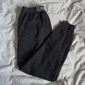 Svarta mjukisbyxor från Calvin Klein - Säljer ett par svarta mjukisbyxor från Calvin Klein. De har en elastisk midja med märkets logga och ribbade muddar vid bensluten. Perfekta för en avslappnad stil.